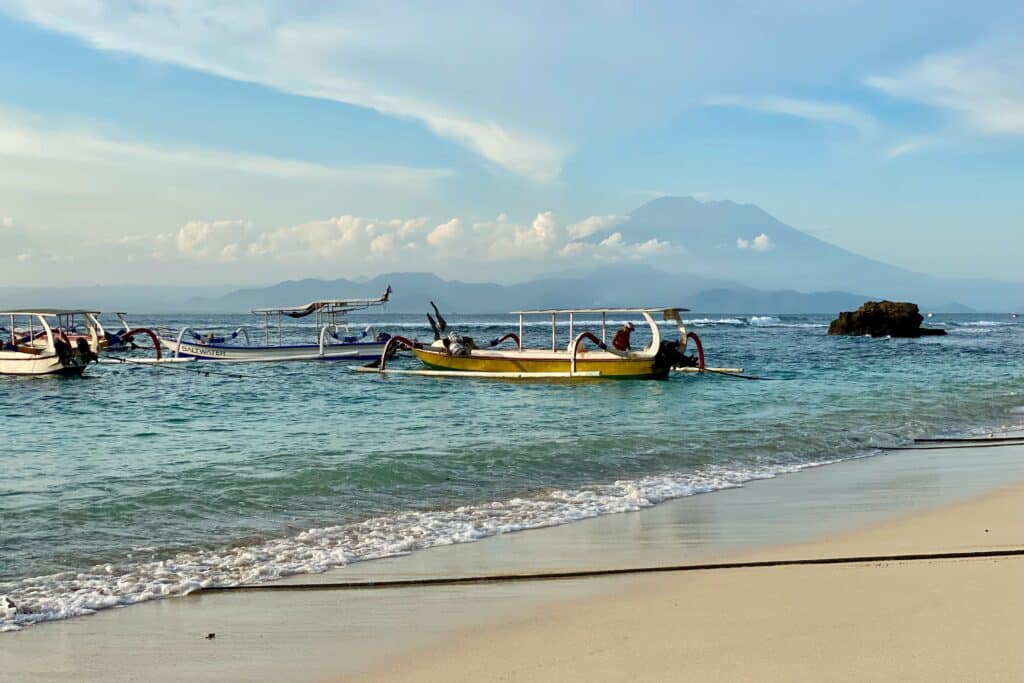 A beach with boats an a volcano in the background